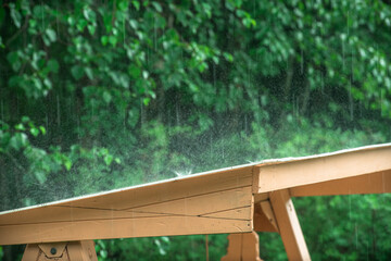 The rain is drumming on the white roof,splashes of water are flying around on a green summer background.