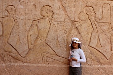 Young girl standing in front of a wall with prisoners carving in Abou simbel in Aswan in Egypt