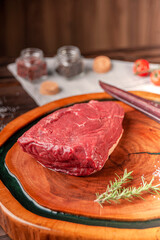 Raw cap rump beef (brazilian picanha) on a wood cutting board with rosemary branch and spices.