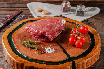 Raw cap rump beef (brazilian picanha) on a wood cutting board with rosemary branch, tomatoes and spices.