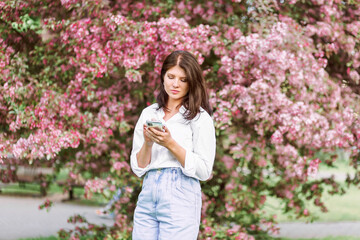 Woman with phone outdoors. Girl with pink coat using mobile in park.