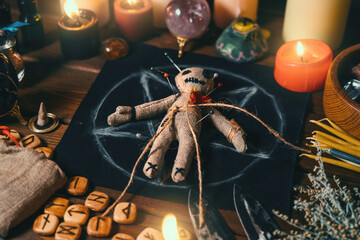 Voodoo doll studded with needles with pierced red rag heart on pentagram and around burning candles. Spooky or eerie magical esoteric ritual.