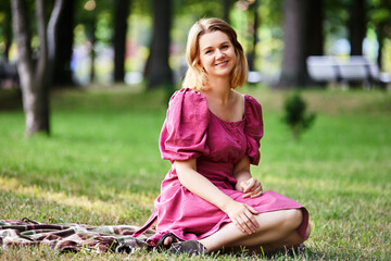 Happy woman in summer dress sits on grass in park.