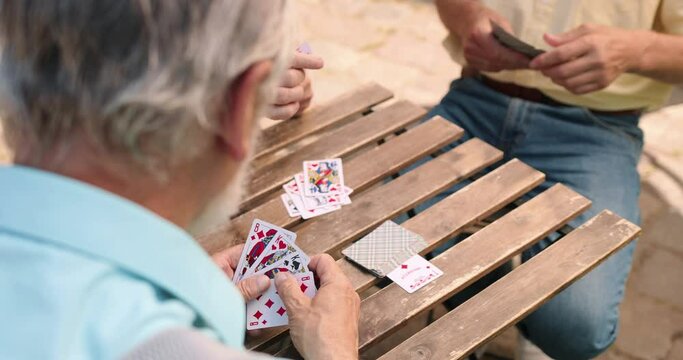 Cropped view of the old caucasian man choosing a card for his turn while his friends making the move. Outdoor.