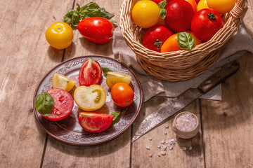 Obraz na płótnie Canvas Ripe assorted tomatoes with fresh basil in a wicker basket