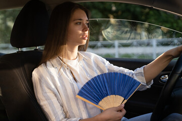 Exhausted young woman driver with hand fan suffering from heat in car, has problem with a...