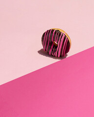 A colorful food gravity photo of a chocolate glazed donut with pink decoration and pink background