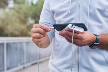 Man charges a smartphone with a power bank in hand. Portable charger for charging gadgets.