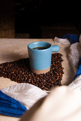taza de café azul sobre granos de café en fondo de mármol con telas azules y blancas