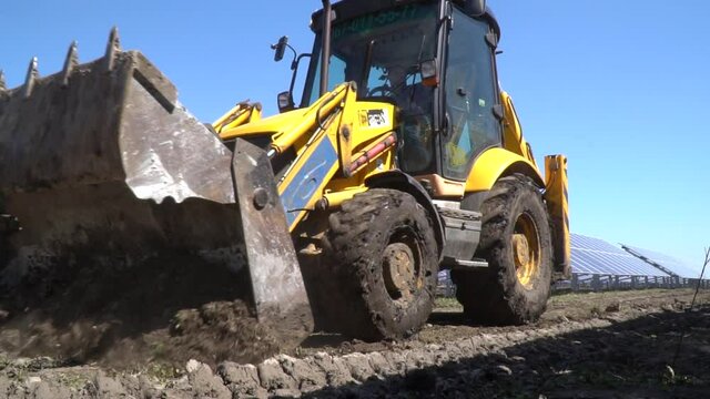 Modern excavator is driving on a road next to the solar panels, power station