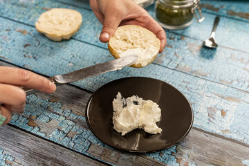Woman's hands spreading cream cheese with a knife on a muffin on the blue table