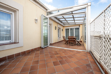 Dining table and chairs in part of the covered terrace of a large urban terrace with blue sky