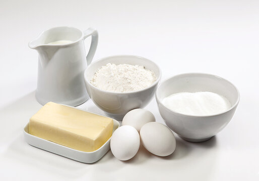 Ingredientes para bolo, ovos, farinha de trigo, açúcar, leite e manteiga no fundo branco para recorte.
