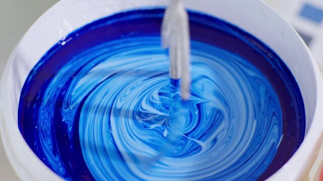 mixing building materials for painting walls, worker mixes blue and white paint in bucket with whisk and drill to renovate room