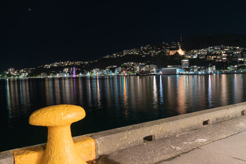 Urban night lights across bay with St Gerard’s church illuminated on hillside from wharf with...