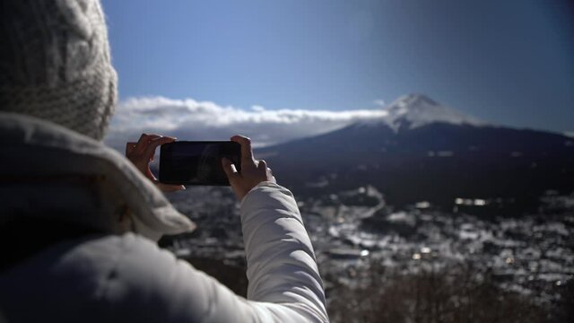 Asian woman take picture with smartphone to the beautiful Fuji mountain with snow cover on the top at Japan. Tourist photographing with the phone a beauty japanese landscape at winter seasons -Dan