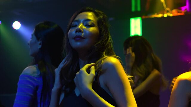 Group of Confidence Asian woman dancing to dj club music with illuminated neon night lights at night club. Fashionable female friends enjoy and having fun nightlife dance party together at nightclub.