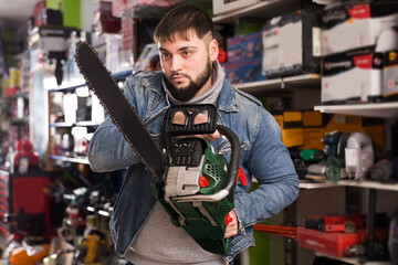 Adult serious male is standing with new chainsaw in tools store