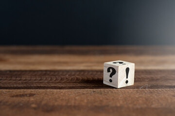Wooden cube with question mark and exclamation point on wooden table. Concept of uncertainty, faq...