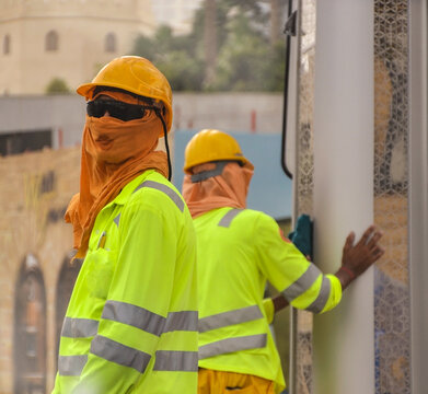 Two blue-collar workers wearing helmets and yellow jackets working under the heat in Doha, Qatar. 