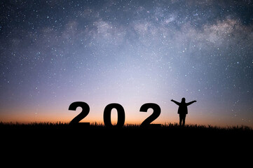 Silhouette of young woman raising hands prepare to welcome the new year 2022 and looking view night sky, star and milky way alone on top of the mountain. She was glad that the new year was coming.