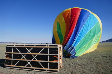 Hot air balloon deflated on ground with basket in foreground