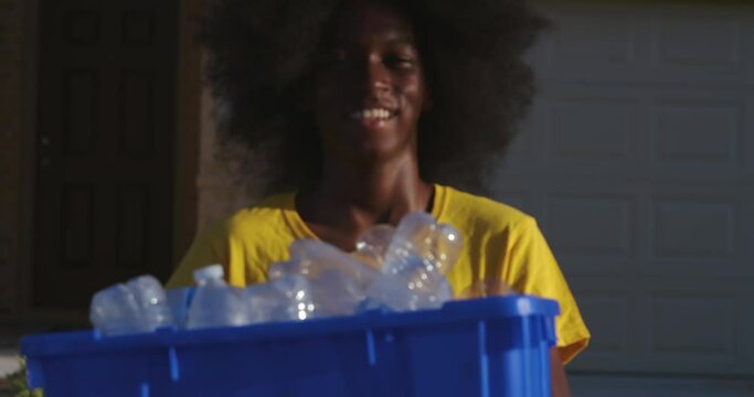 African American adolescents with huge Afro smiling as he hold recycle bin full of plastic bottles
