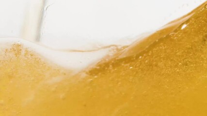 Macro shot filling a glass of beer creating lot of bubbles on white backdrop