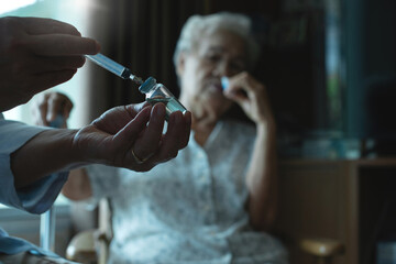 Doctor giving injection coronavirus vaccine to the elderly patient, elderly wearing medical mask, general practitioner visiting her at home, elderly health care concept, selective focus