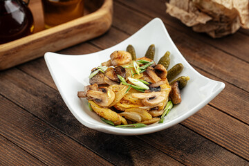 Roasted potatoes with mushrooms and pickles on the wooden background