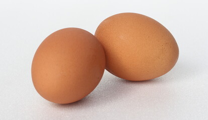 Two chicken eggs laid on a white foam surface.
