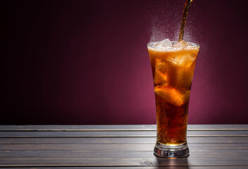 Pour sparkling water in a cola glass with ice cubes on a wooden table. on a dark black background.