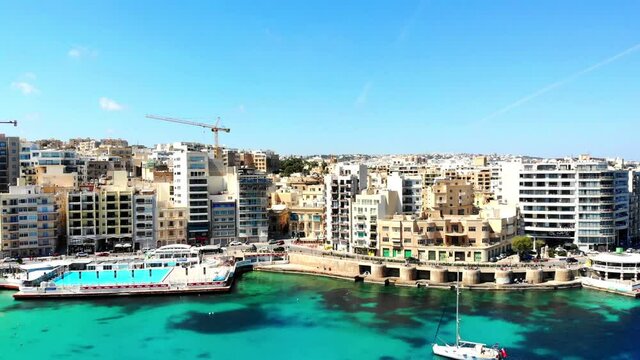 Drone flying backwards over Balluta Bay Beach. Breathtaking view of St. Julians city in Malta island.