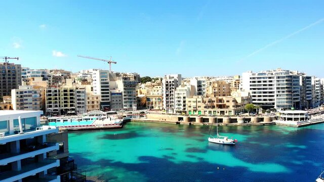 Drone downward movement shot of St. Julians city, Balluta Bay Beach. Boats and yachts are standing still in water of Maltese island.