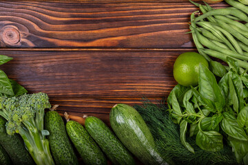 Fresh ingredients for cooking. Seasoning frame with place for inscription. Frame of green vegetables on wooden background. Top view of green vegetables. Healthy summer vegetables on dark wooden table