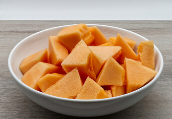Sweet Melon slices in a white bowl on wooden table. Fresh fruit