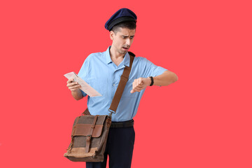 Shocked young postman looking at wristwatch on color background