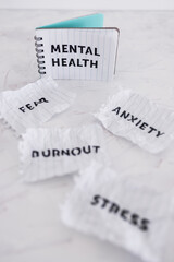 Fototapeta na wymiar Mental health text on notepad surrounded by Fear Anxiety Stress and Burnout words on scrunched up pages, psychology concept