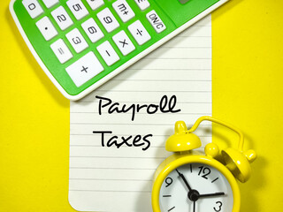 Business concept.Text Payroll Taxes writing on notepaper with alarm clock and calculator on a yellow background.