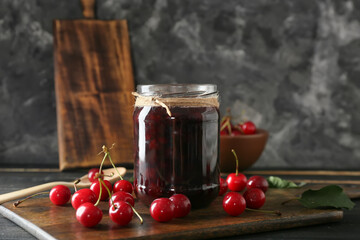 Jar with tasty cherry jam on dark background