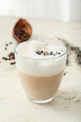 Glass of tasty lavender latte and flowers on light background