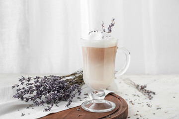Glass of tasty lavender latte and flowers on light background