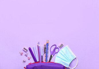 Pencil case with set of stationery and medical mask on color background