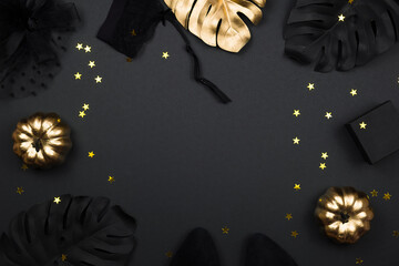 Halloween party collection female outfit accessories on black background: hat with veil, garter belt, gifts. Black and gold pumpkins, flat lay, top view, copy space.