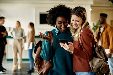 Cheerful female students use smart phone and have fun in hallway at the university,