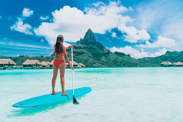 SUP Tahiti paddleboard woman standing on stand-up board paddling over turquoise ocean at luxury beach resort hotel on Bora Bora island, French Polynesia. - obrazy, fototapety, plakaty