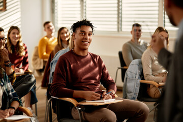 Happy African American college student listens lecture in classroom.
