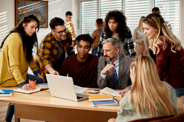 Mature teacher and group of his students use laptop at the university,