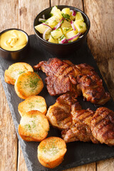 Schwenker or Schwenkbraten is a marinated pork neck steak  served with potatoes salad, mustard and toast closeup in the slate board on the table. Vertical