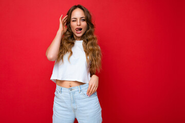 Shot of young emotional happy sexy positive pretty blonde woman wearing white t-shirt isolated on red background with empty space